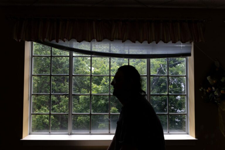 a silhouetted man stands in front of a window.