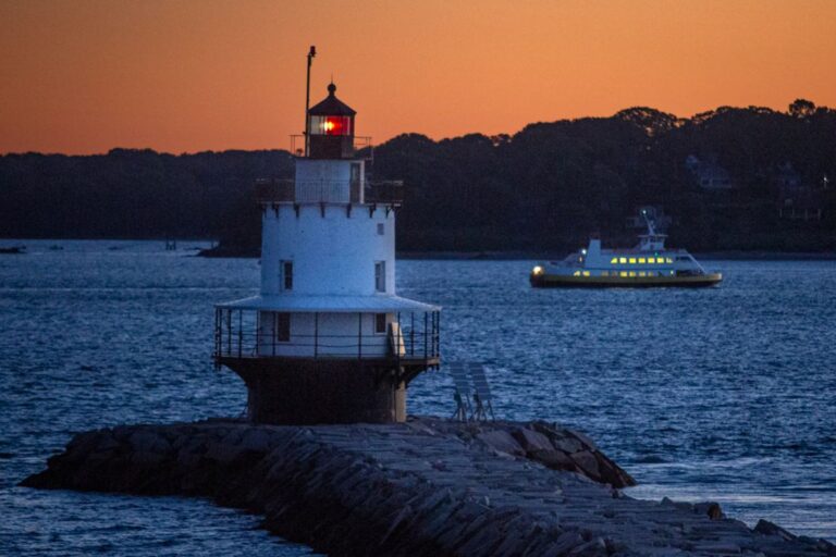 A ferry passes behind a lighthouse.