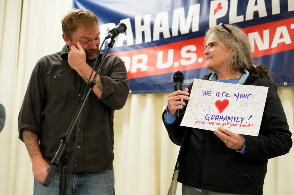 Graham Platner wipes a tear from his eye as he is presented with a signed card of support that reads We are your Grahamily and we've got your back.