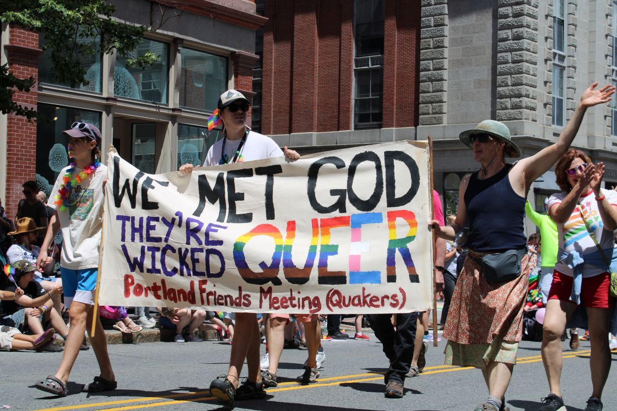 people marching with a banner that reads we met god they're wicked queer
