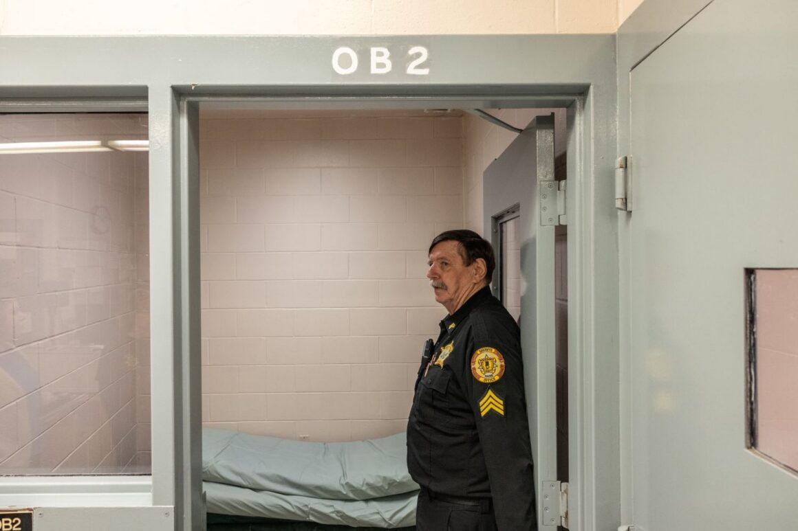 A corrections officer stands to the side in a doorway