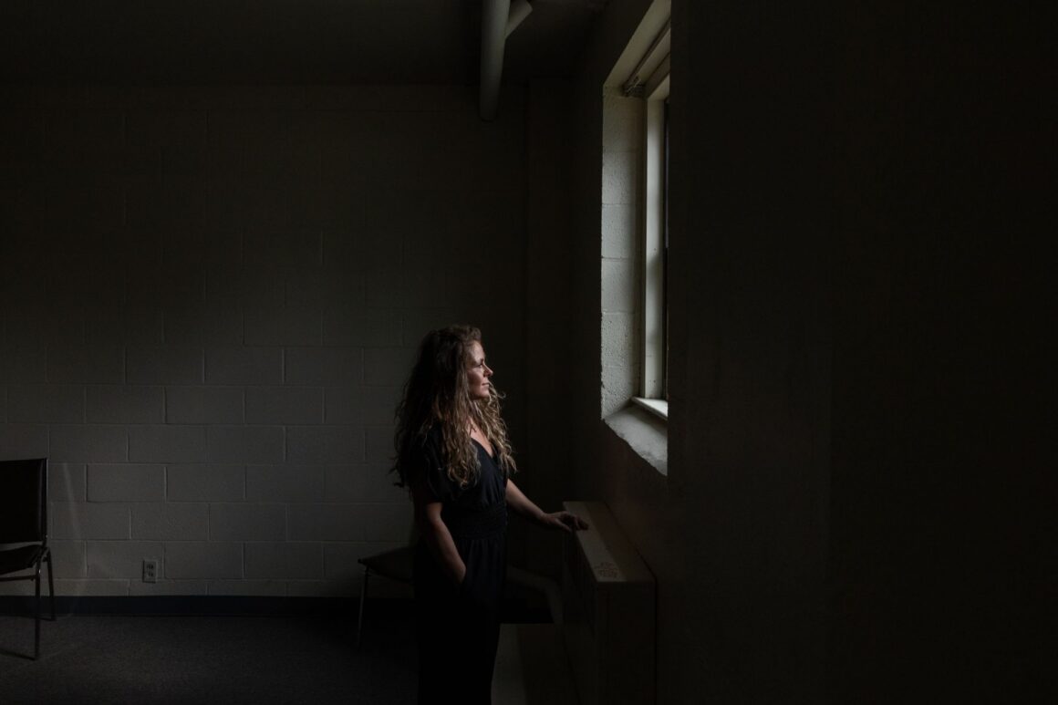 Audrey Condon looks out a window in a dark room.