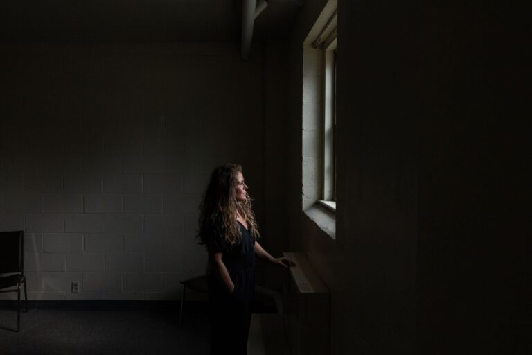 Audrey Condon looks out a window in a dark room.
