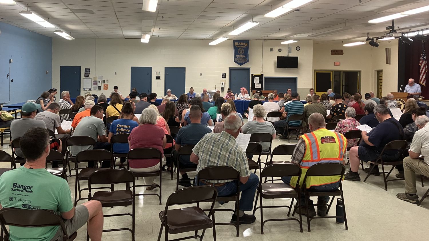 a crowd of people and school board members seated for a meeting.