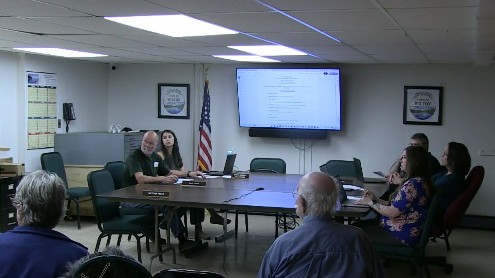 select board members sit a table at the front of the room.