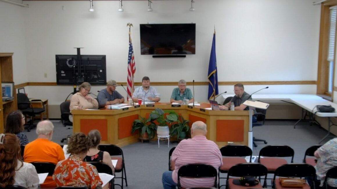 members of the select board sit around a table during a meeting.