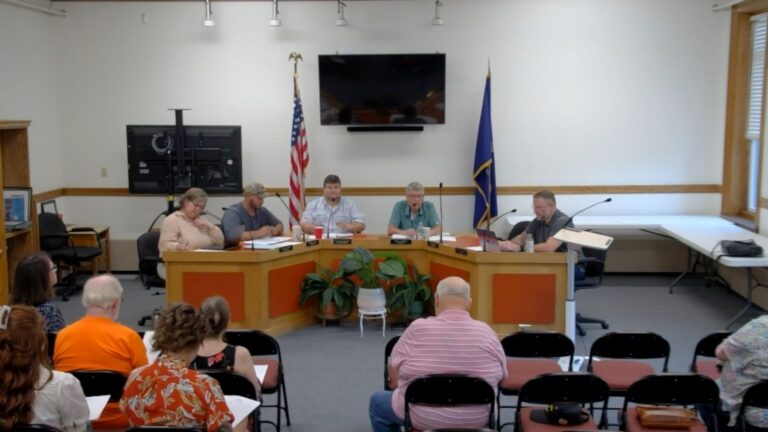 members of the select board sit around a table during a meeting.