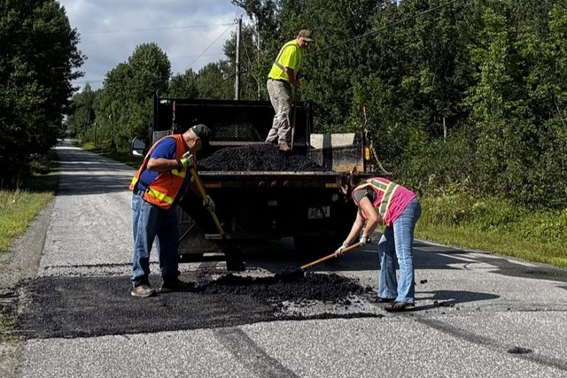 a trio of town employees fill a pothole.