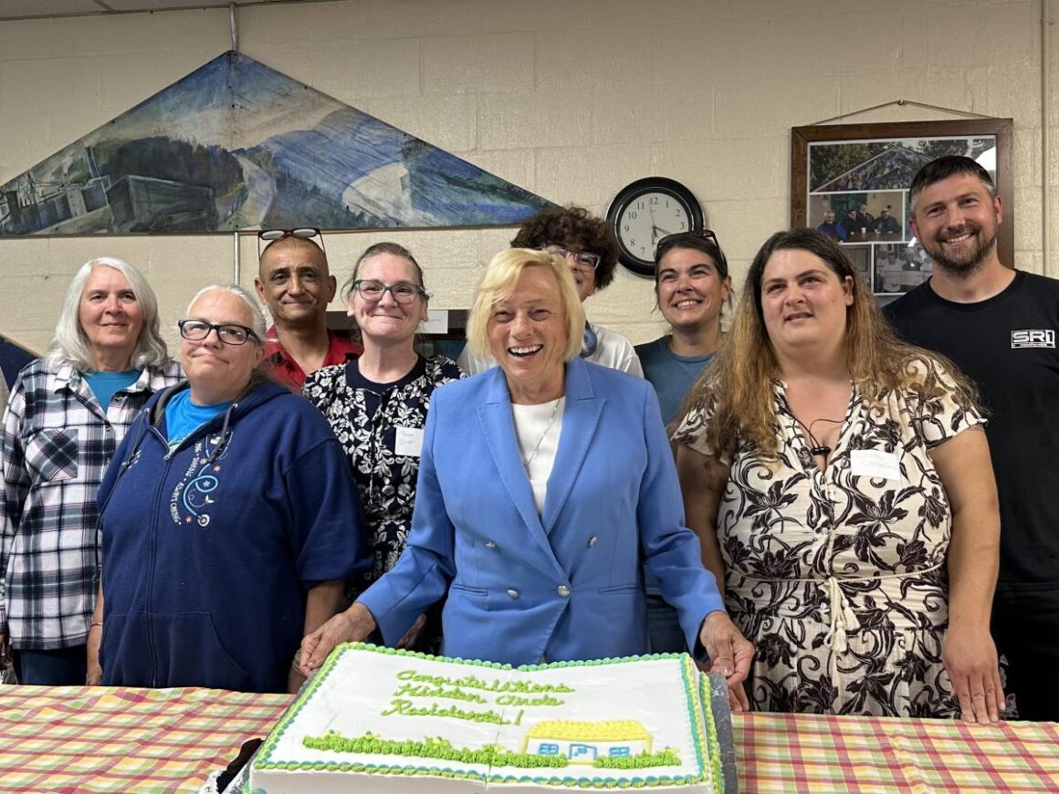 residents and governor janet mills gather around a cake for a photo.