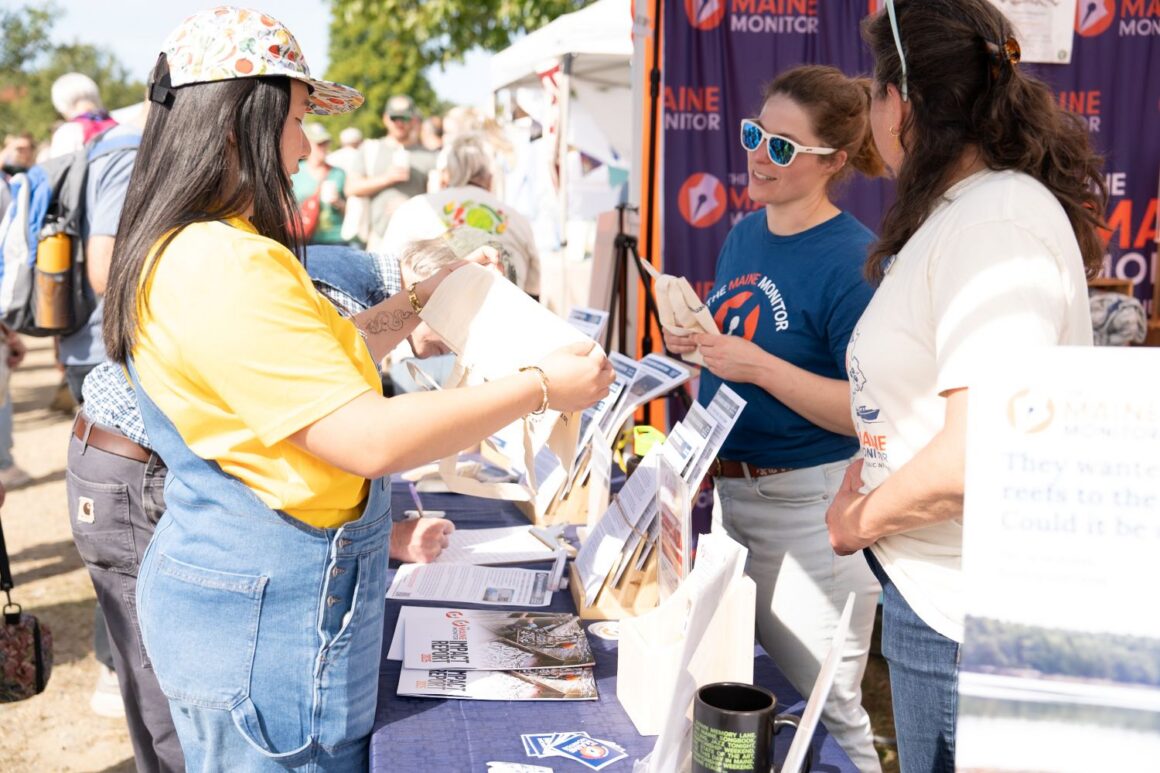 Monitor staffers speak with a fair attendee at the monitor's table.