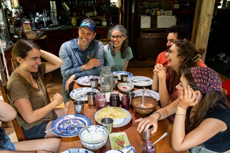 The Hughes family laughs while sitting around a dining table during a meal.