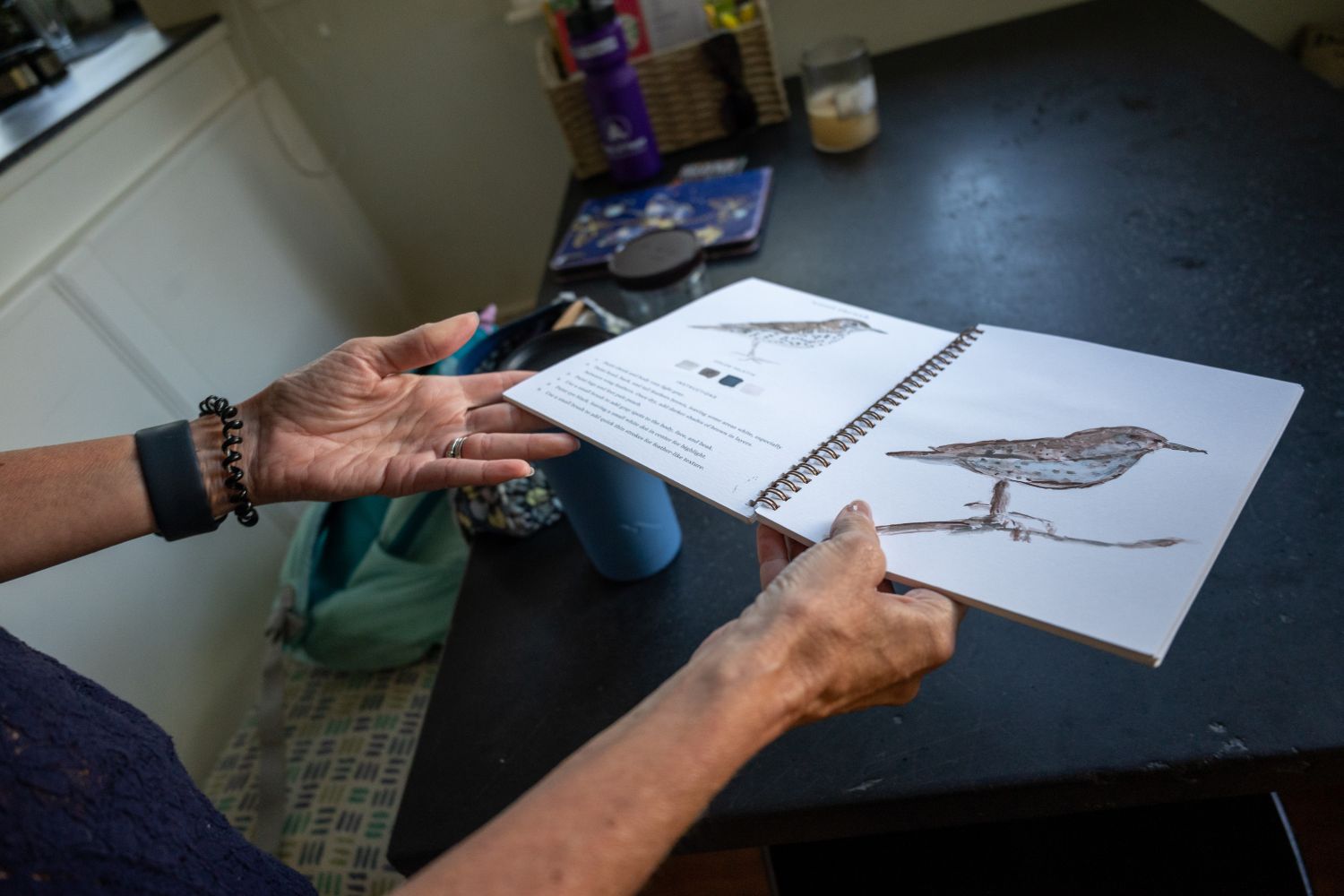 tracey collins holds open a book of her watercolor paintings, this one of a bird