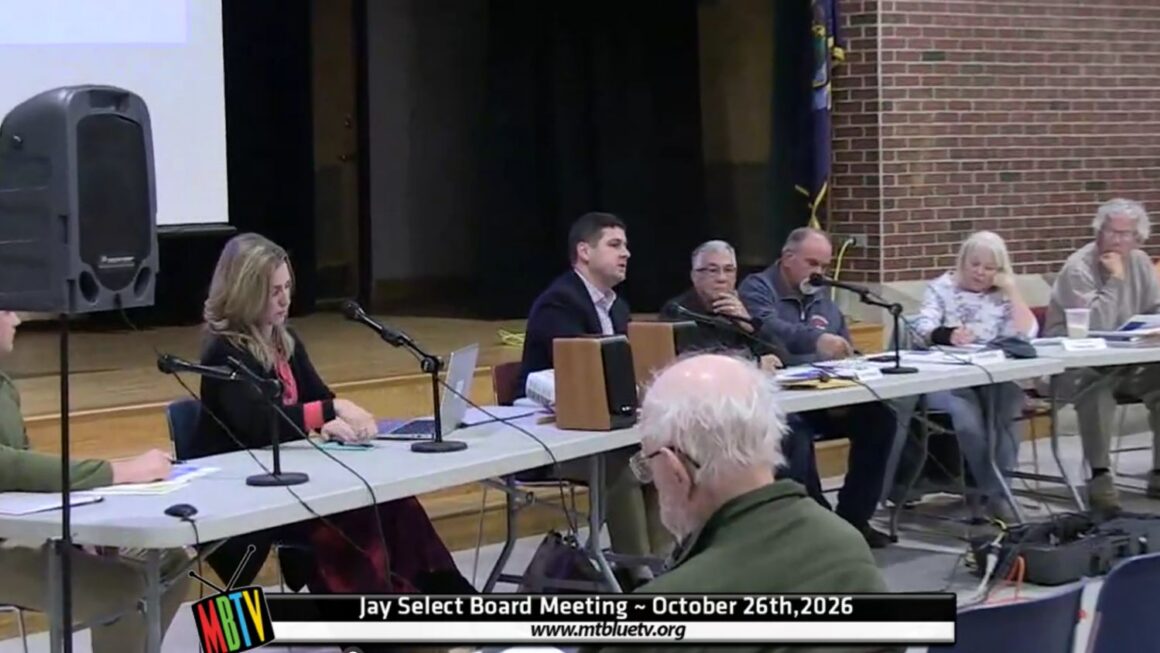 select board members sit at a table during a meeting.
