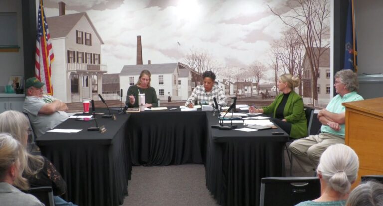 select board members sit around a u-shaped table during a meeting.