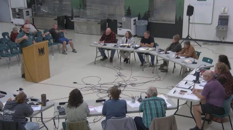 school board members listen to a speaker standing at a podium